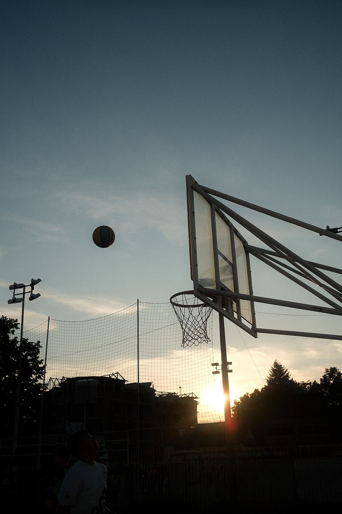A basketball dropping through an outdoor hoop at sunset